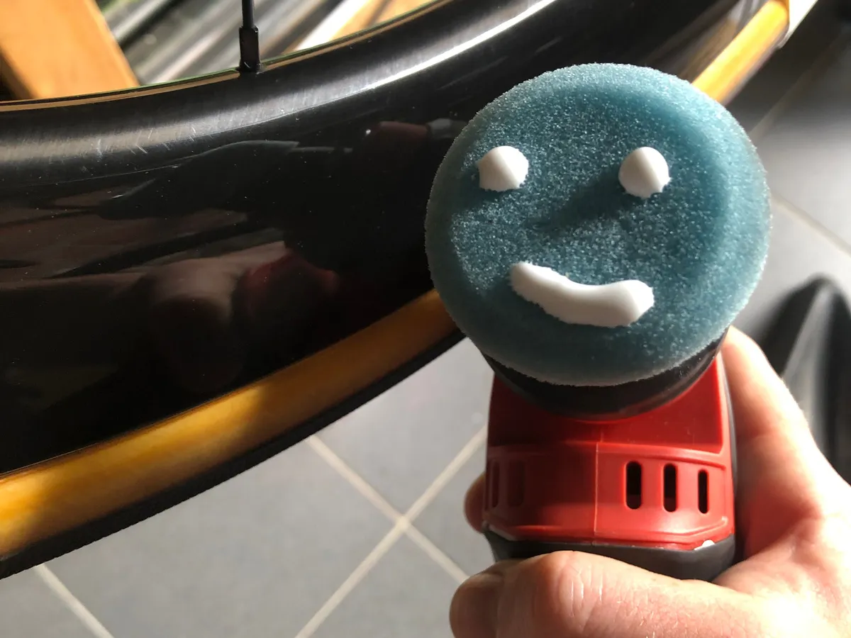 Hand met een poetsmachine aan een wielset, het pad heeft een lachend gezichtje