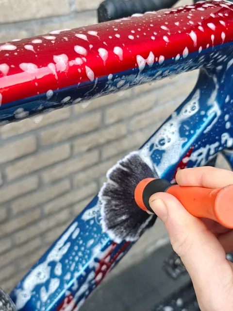 Hand met een zachte borstel op een rood-blauw frame vol schuim